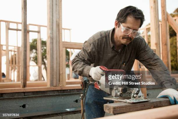 mixed race construction worker using saw on lumber - hispanic construction worker stock-fotos und bilder