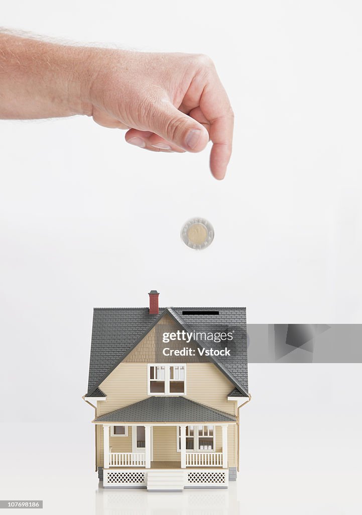 Close up of man's hand throwing coin into model house