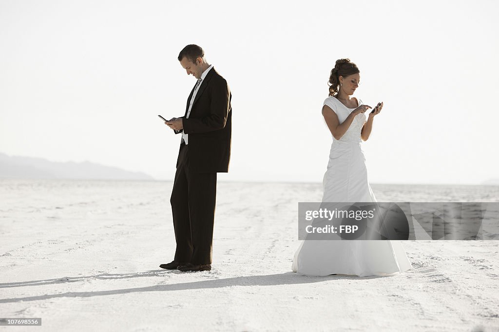 USA, Utah, Boneville Salt Flats, Bride and groom texting in desert
