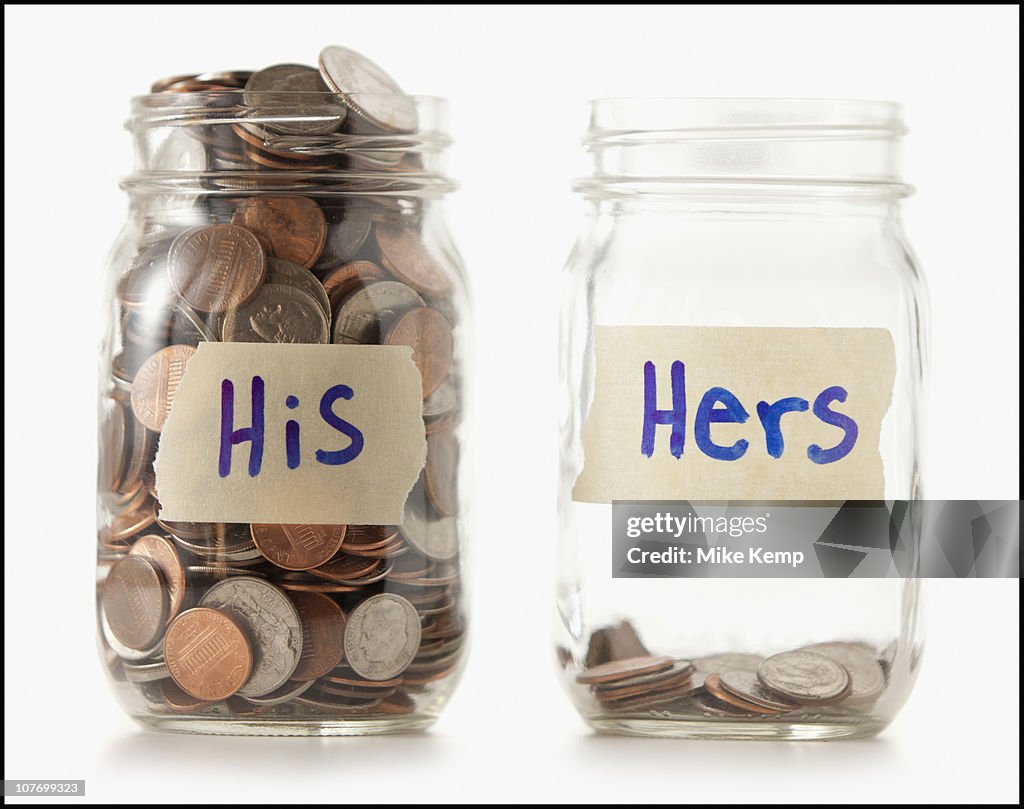 Studio shot of two jars with coins labeled ""Hers"" and ""His