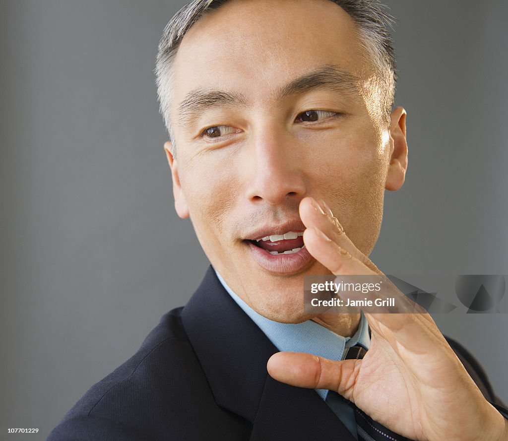Businessman covering face and whispering, studio shot