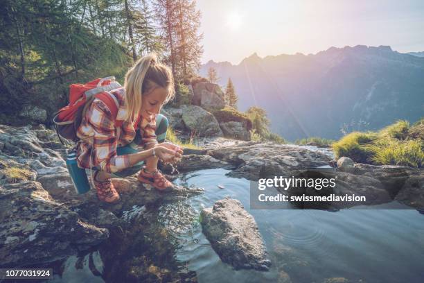 wanderer weibliche trinkwasser auf bergweg aus frischen stream - gebirgsfluss stock-fotos und bilder