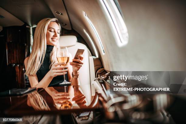 hermosa rubia empresaria bebiendo vino y usando un teléfono inteligente en un avión privado - primera clase fotografías e imágenes de stock