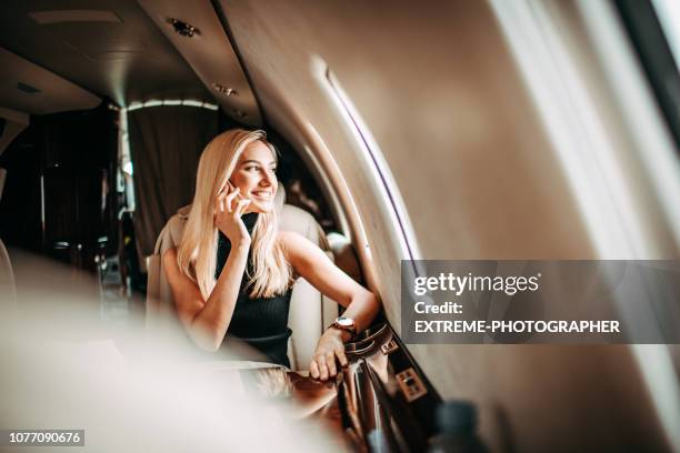 beautiful young businesswoman talking on a mobile phone while traveling in a private airplane - high society imagens e fotografias de stock