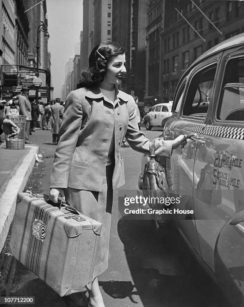 Woman carrying a suitcase getting in to a taxi in New York City circa 1950.