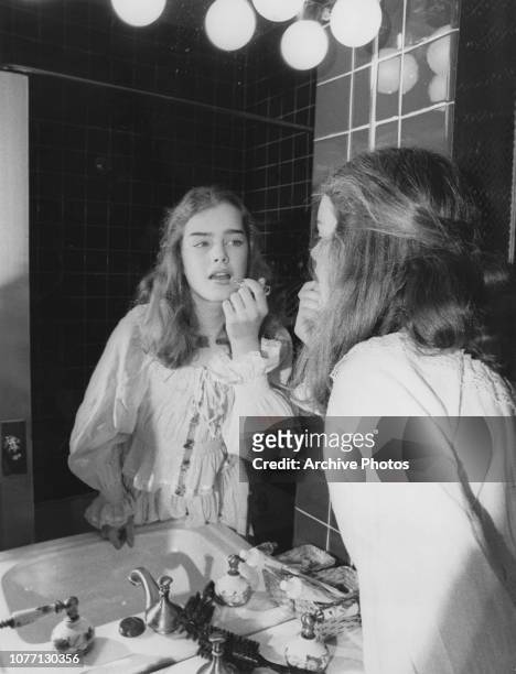 American actress Brooke Shields applies lipgloss in a bathroom mirror, circa 1980.