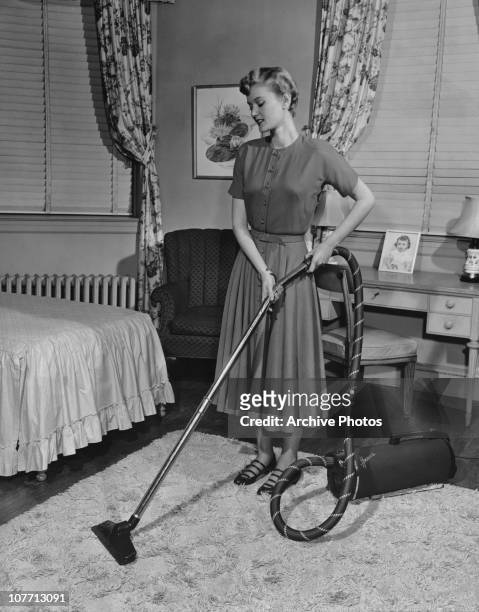 Woman cleaning a bedroom carpet with a vacuum cleaner circa 1940's.