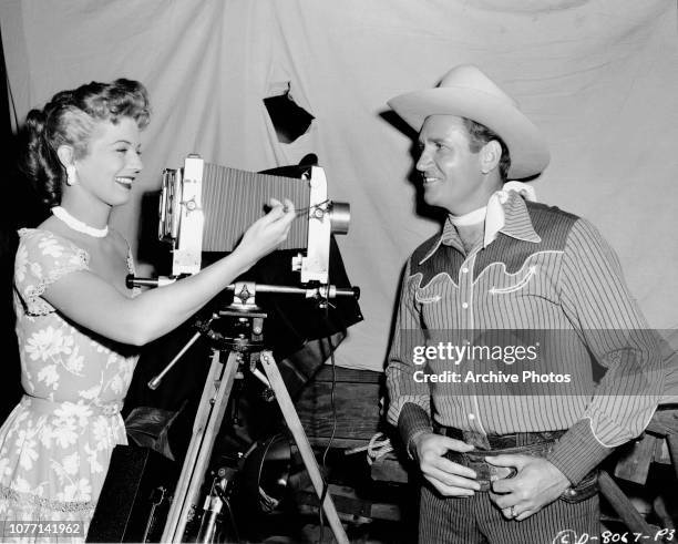 American actress Gail Davis takes a photograph of regular co-star Gene Autry with an old-fashioned camera, circa 1953.