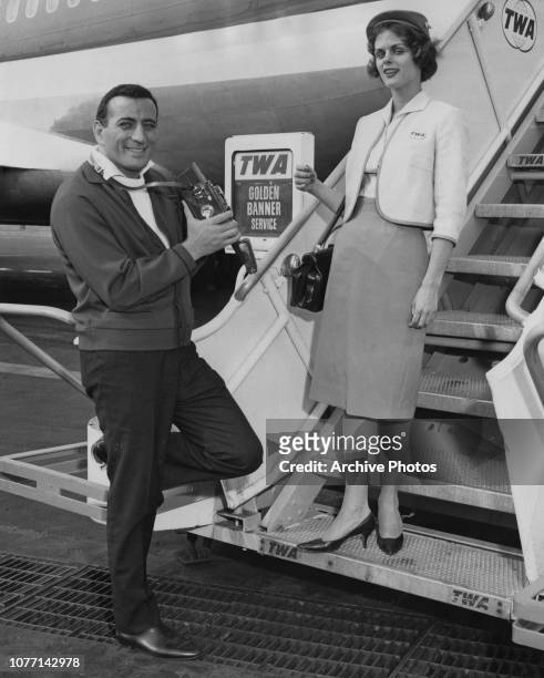 American singer Tony Bennett leaves New York International Airport on TWA's Golden Banner Service, 13th June 1961. He takes a picture of air hostess...