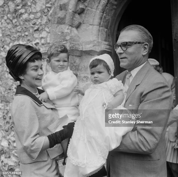 English actors Joan Plowright, holding son Richard, and Laurence Olivier pictured attending the christening of their daughter Tamsin at a church in...