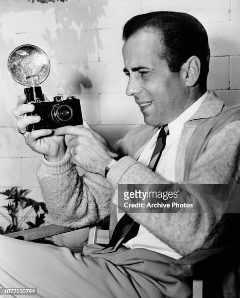 American actor Humphrey Bogart holding a camera on the set of the film 'They Drive by Night', circa 1940.