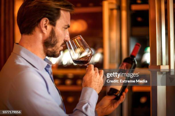man tasting and degustating wine in front of a wine cooler - wine rack stock pictures, royalty-free photos & images