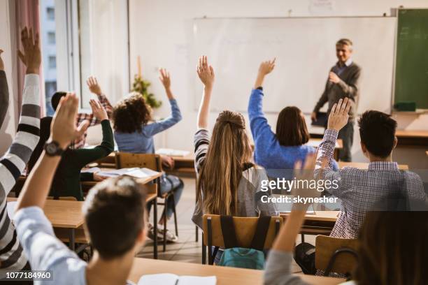 achteraanzicht van middelbare scholieren verhogen handen op een klasse. - classroom stockfoto's en -beelden