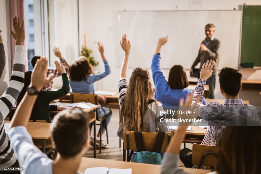 Baksidan på high school-elever att höja händerna på en klass.