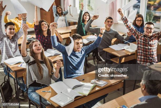 happy students throwing papers while celebrating the end of a school year in the classroom. - finale celebration stock pictures, royalty-free photos & images