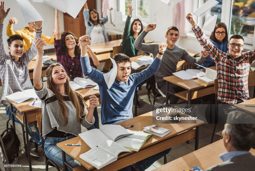 Glada studenter kasta papper samtidigt fira slutet på ett läsår i klassrummet.