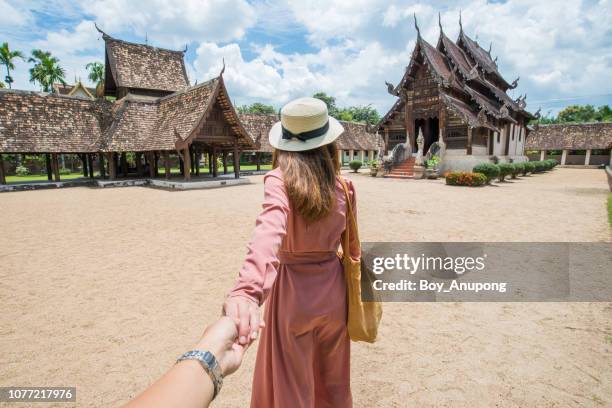 back view of asian tourist holding her boyfriend hand and traveling in wat inthrawat temple in chiang mai, thailand. - lanna stock pictures, royalty-free photos & images