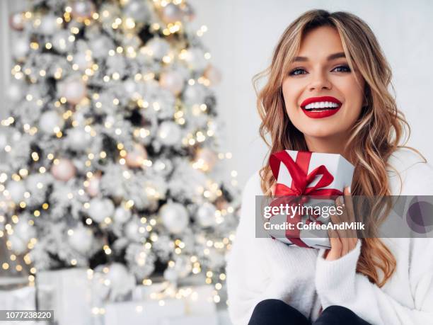 クリスマスツリーの近くの居心地の良い雰囲気の中に座っている美しい女の子 - 赤の口紅 ストックフォトと画像