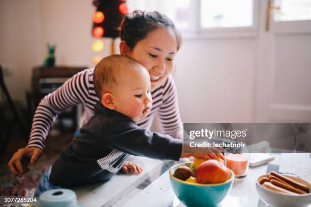 junge asiatische mutter gibt nahrung für ihr baby boy - child eating a fruit stock-fotos und bilder