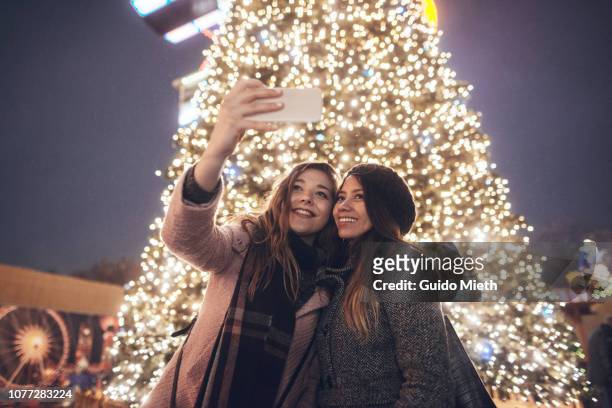 girlfriends doing selfie in front of christmas tree. - christkindlmarkt stock-fotos und bilder