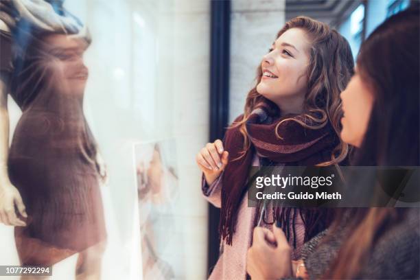 girlfriends looking into shopping window. - window shoppen stockfoto's en -beelden