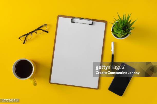 clipboard with white paper, mobile phone and coffee mug on yellow background - notepad table stock pictures, royalty-free photos & images