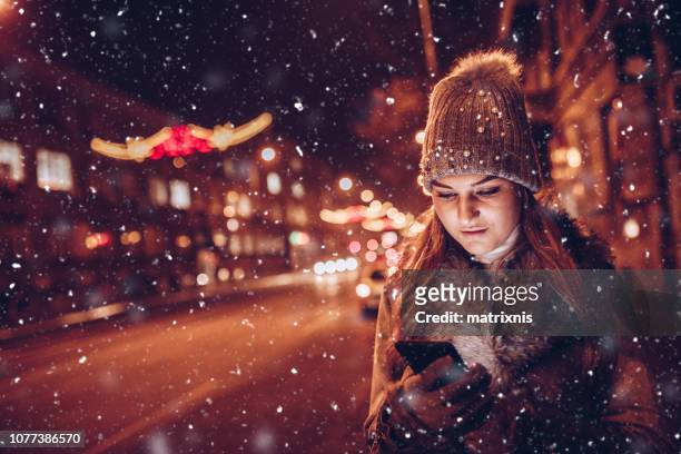 young female in the city under night city lights waiting for her ride - woman snow outside night stock pictures, royalty-free photos & images