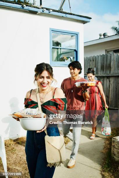 laughing friends walking into backyard with trays of food for barbecue on summer evening - summer party arrivals stock-fotos und bilder