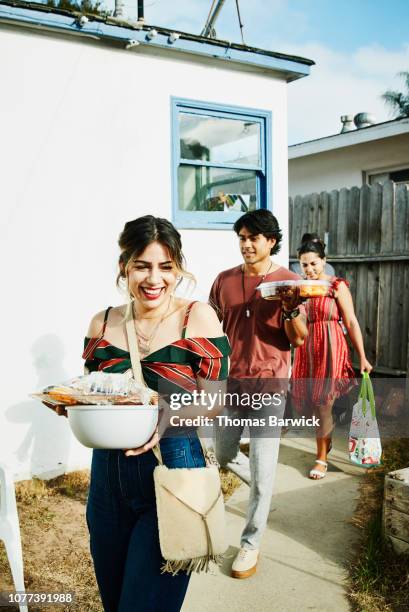 laughing friends walking into backyard with trays of food for barbecue on summer evening - carrying stock pictures, royalty-free photos & images