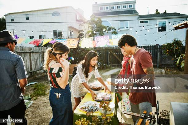 group of friends putting trays of food on table in backyard before summer evening barbecue - day california arrivals stockfoto's en -beelden