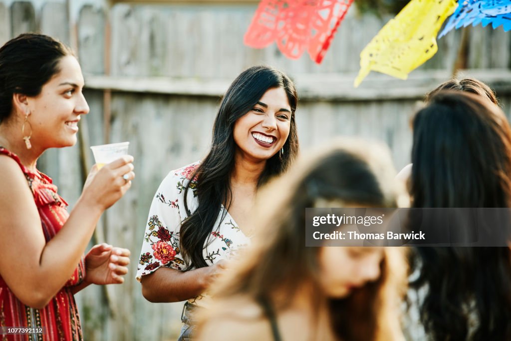 Laughing group of female friends sharing drinks during backyard barbecue on summer afternoon