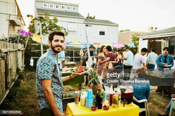 portrait of man bringing food to table during backyard party with friends on summer evening - barbecue cibo foto e immagini stock