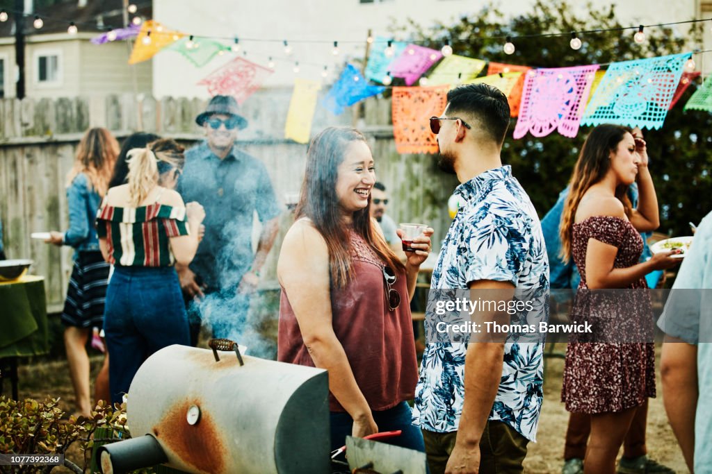 Laughing woman in discussion with friend during backyard barbecue on summer evening