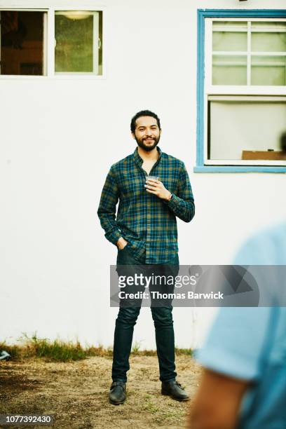portrait of smiling man with drink standing in backyard during party - person standing infront of wall stockfoto's en -beelden
