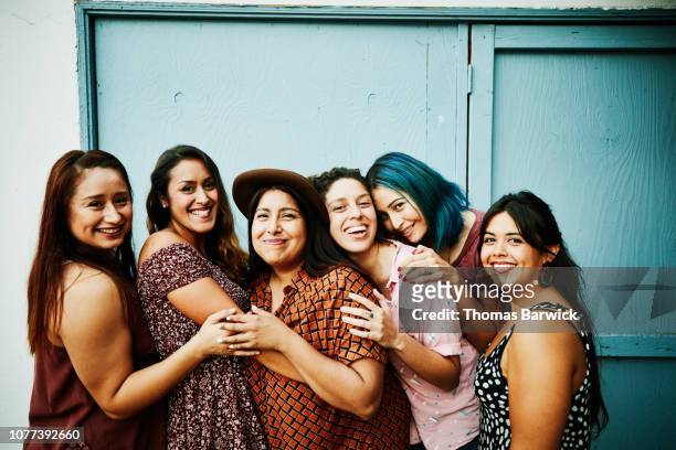 portrait of female friends embracing in front of blue wall - nur frauen stock-fotos und bilder