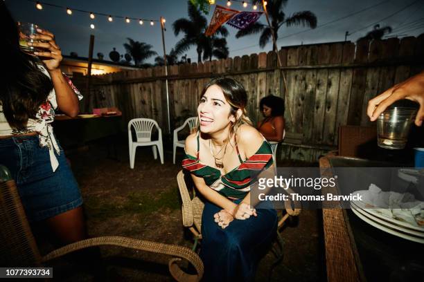laughing woman sitting in backyard with friends during party on summer evening - summer party lights stock-fotos und bilder