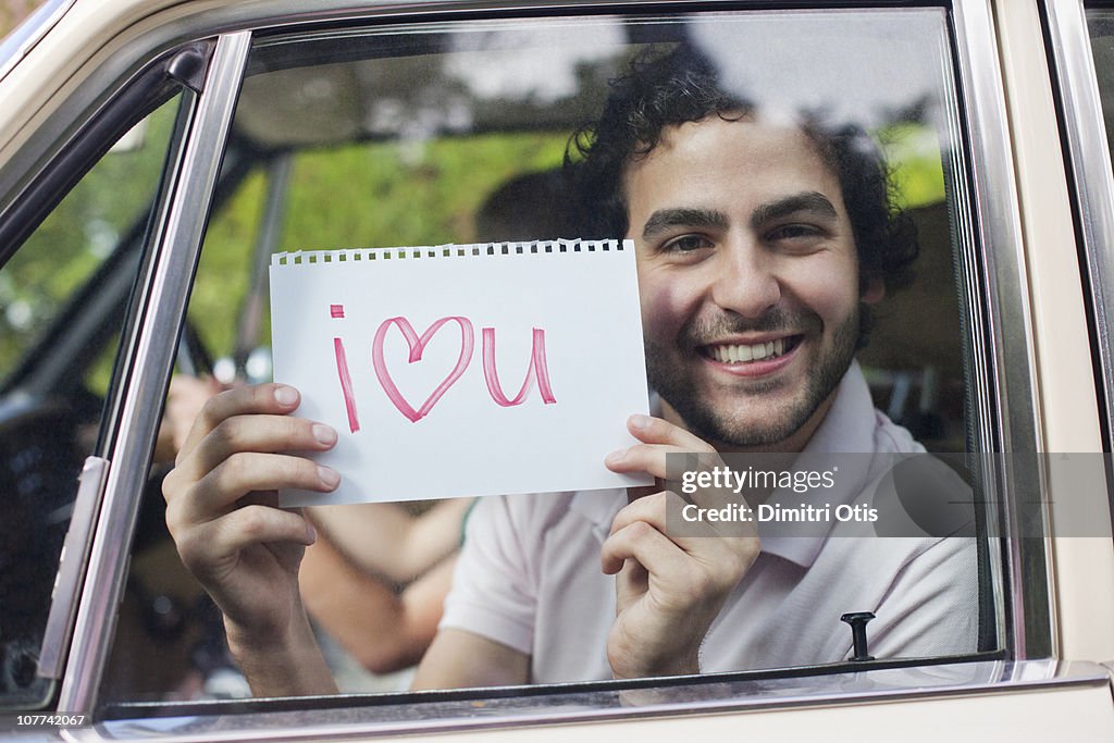 Man in car holding sign saying 'I love you'