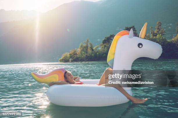 junge frau auf aufblasbaren einhorn, die spaß am schönen see in der schweiz - menschen reisen urlaub konzept - unicorn stock-fotos und bilder