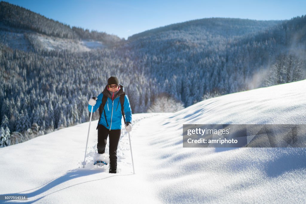 Woman in warm winter sport clothes enjoying snowshoe hike in deep snow on sunny winter day in rural landscape