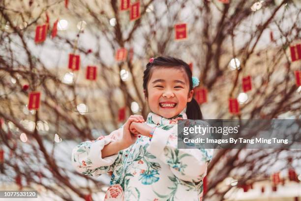 lovely little girl with kung hei fat choi hand gesture for chinese new year smiling joyfully at the camera in front of a peach blossom tree in chinese new year - 2018 chinese new year stock pictures, royalty-free photos & images