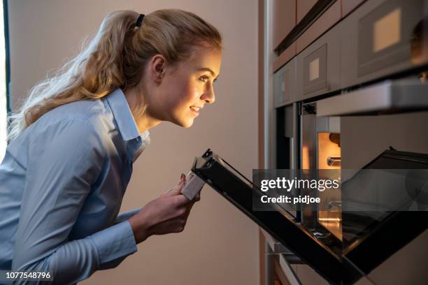 seitenansicht der jungen frau check-essen in den ofen - looking back stock-fotos und bilder