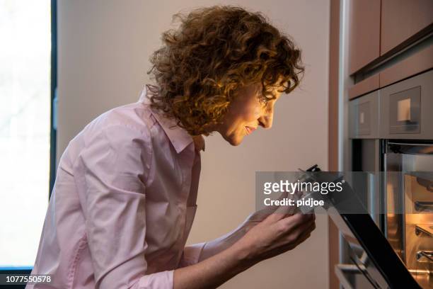 zijaanzicht van vrouw controleren van voedsel in de oven - oven stockfoto's en -beelden