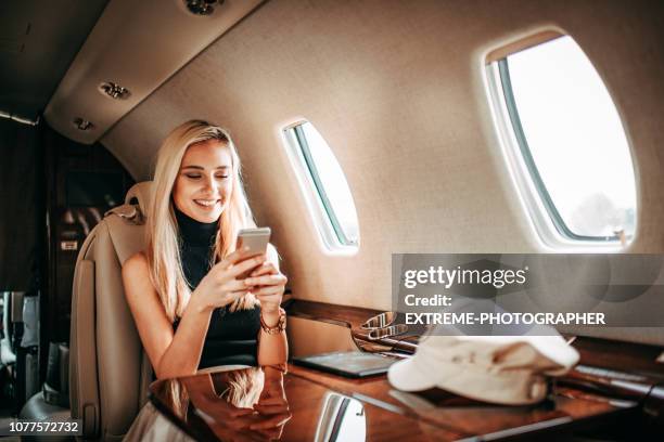 giovane ricca donna bionda che usa un telefono cellulare mentre viaggia su un jet privato - exclusive foto e immagini stock