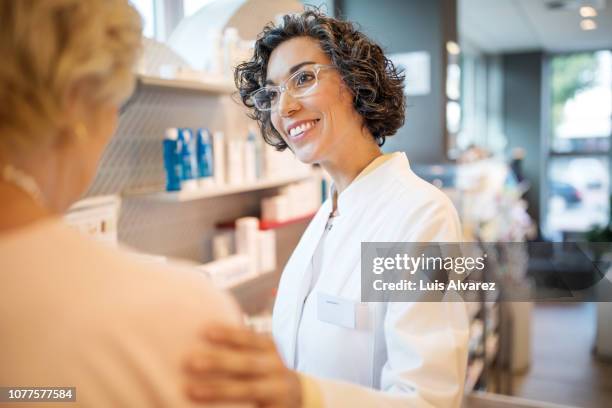 smiling female chemist consoling costumer at pharmacy - pharmacist fotografías e imágenes de stock