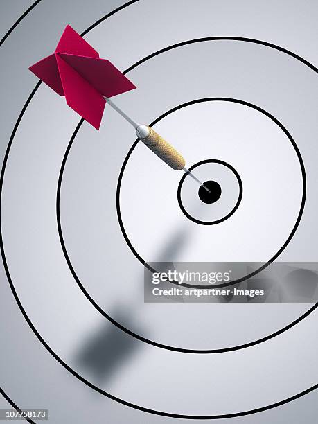 a dart hitting bulls eye on a dartboard - zielscheibe stock-fotos und bilder