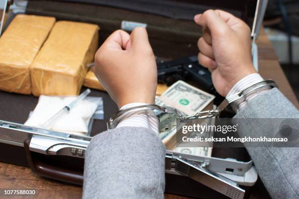 the drug dealer was arrested in handcuffs, drugs money and gun on wooden table in concept about danger and threat of the drug - droga recreativa imagens e fotografias de stock