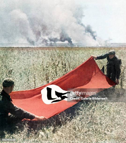 Operation Barbarossa, Two Wehrmacht soldiers are holding a Swastika flag to protect against friendly fire. 1942. Fighting is going on nearby on the...