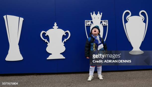 Young Chelsea fan poses for a photograph in front of pictures of trophies The Europa League, FA Cup, Premier League and Champions League outside the...