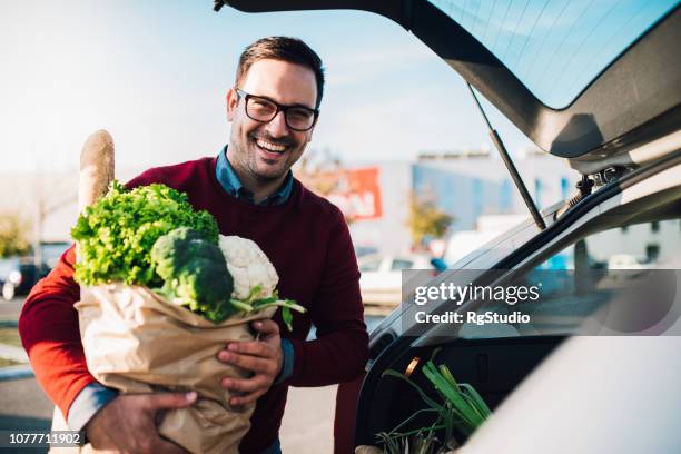 lächelnd jungen mann hält einkaufstüte - car shopping stock-fotos und bilder