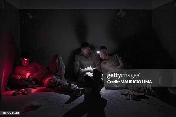 Marine from India Company, 3rd Battalion, 6th Marines uses a headlight set up in red color to read a book while his comrade share their plans for the...